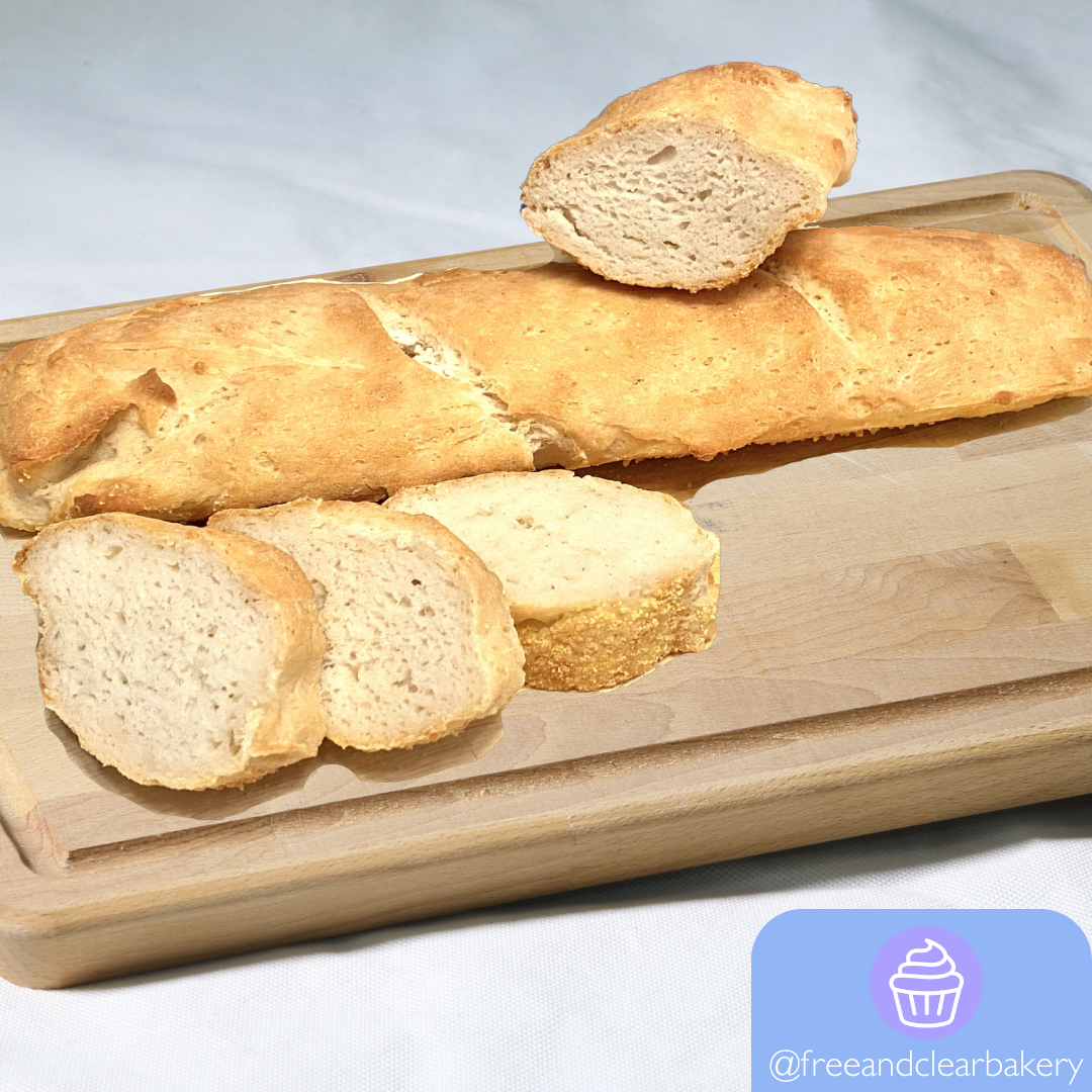 One golden brown French bread baguette on top of a cutting board. Leaning on it is a half baguette, angled to see the perfectly baked inside. In front, three thick slices of baguette arranged aesthetically.