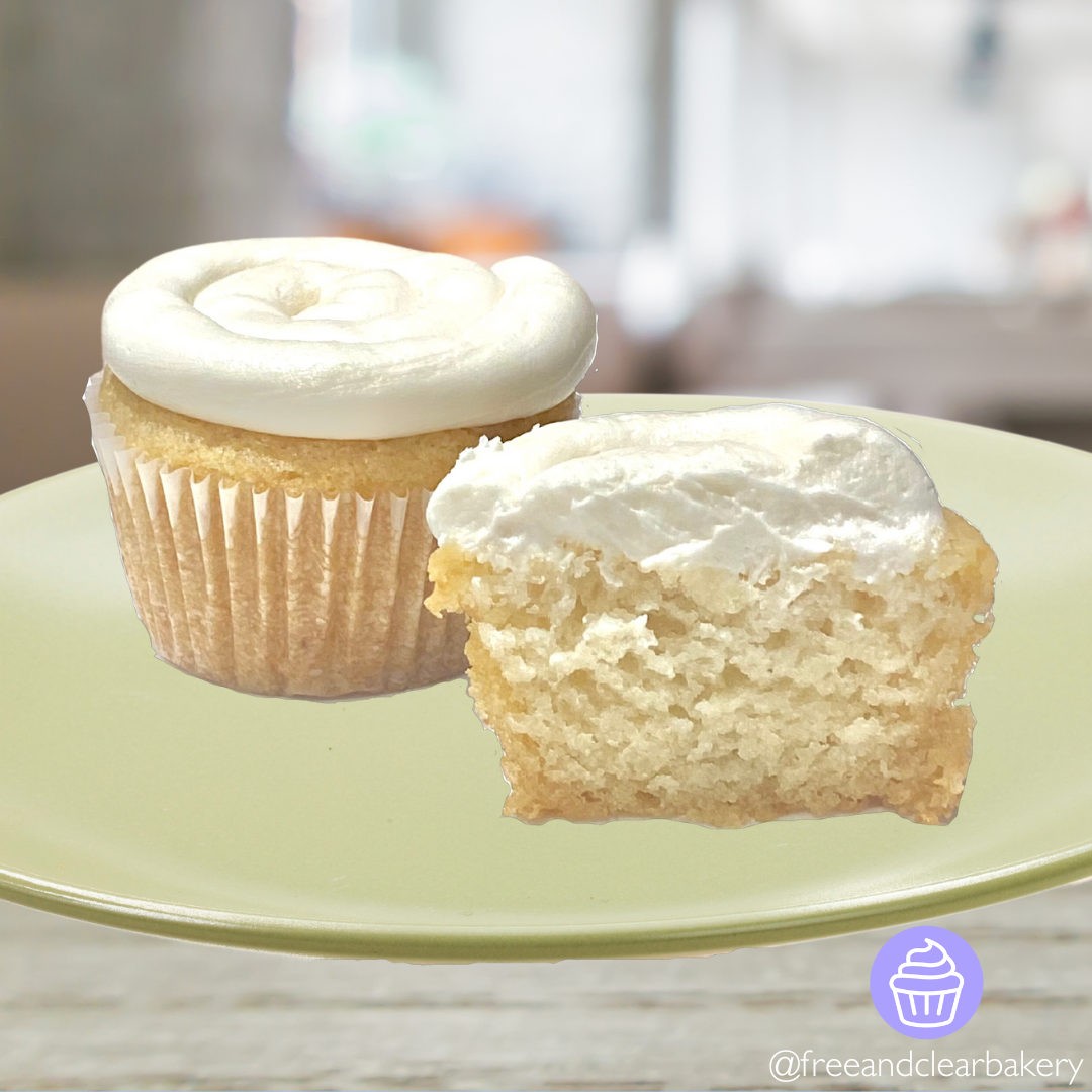 Two beautiful white cupcakes with white frosting, one of them cut in half to show the inside. Both on a light green plate.