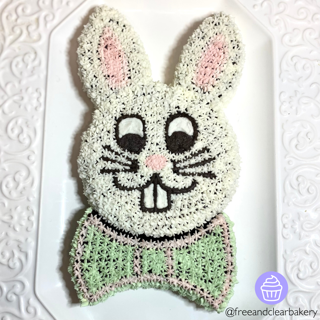 One circle cake makes the bunny face, and another cake is cut into pieces to form the ears and bowtie. All decorated with buttercream dollops to look like an Easter bunny face