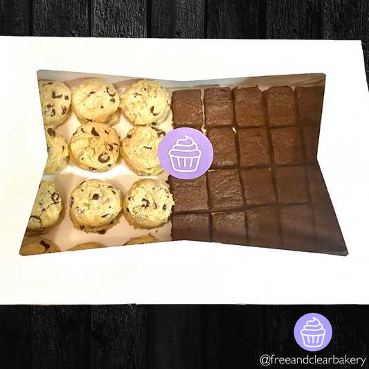 White bakery box with clear window on top and purple circle Free & Clear logo sticker with white outline of cupcake in the center. In the box is 24 chocolate chip cookies and 25 brownies. The box is sitting on a black wooden table.