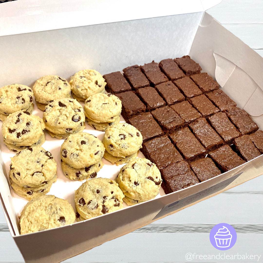 White bakery box opened to show the contents of 24 chocolate chip cookies and 25 brownies. The box is sitting on a white wooden table.