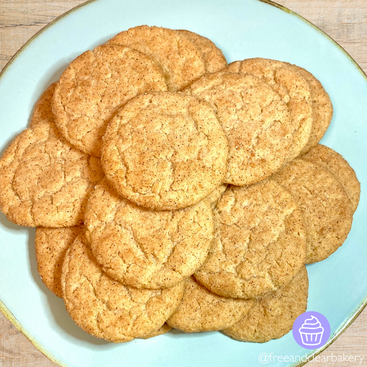 Light blue plate with gold rim, with 20 snickerdoodle cookies arranged in a neat pile. Each cookie is evenly coated with cinnamon and sugar and have a slight crackle effect.