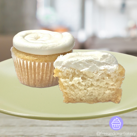 Two beautiful white cupcakes with white frosting, one of them cut in half to show the inside. Both on a light green plate.